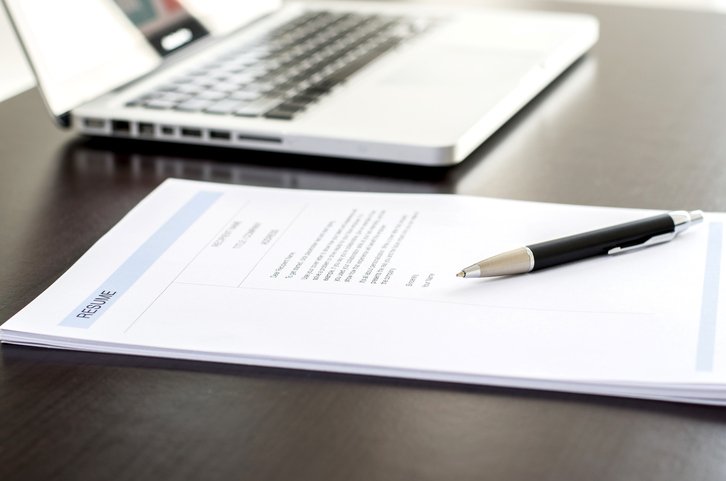 stack of resumes on a table with a pen on top and macbook computer next to them